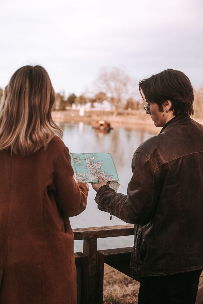 Couple with a map planning a journey by a serene lake in rural setting.